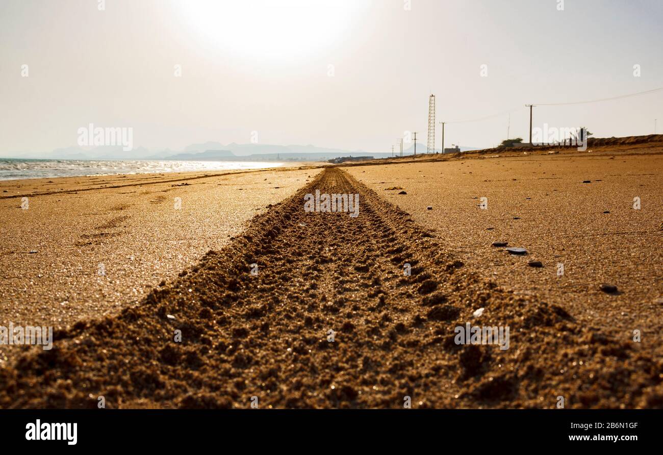 Impronte di pneumatici da motociclista su una spiaggia di sabbia dorata al tramonto. Un battistrada senza fine su fango. Foto Stock