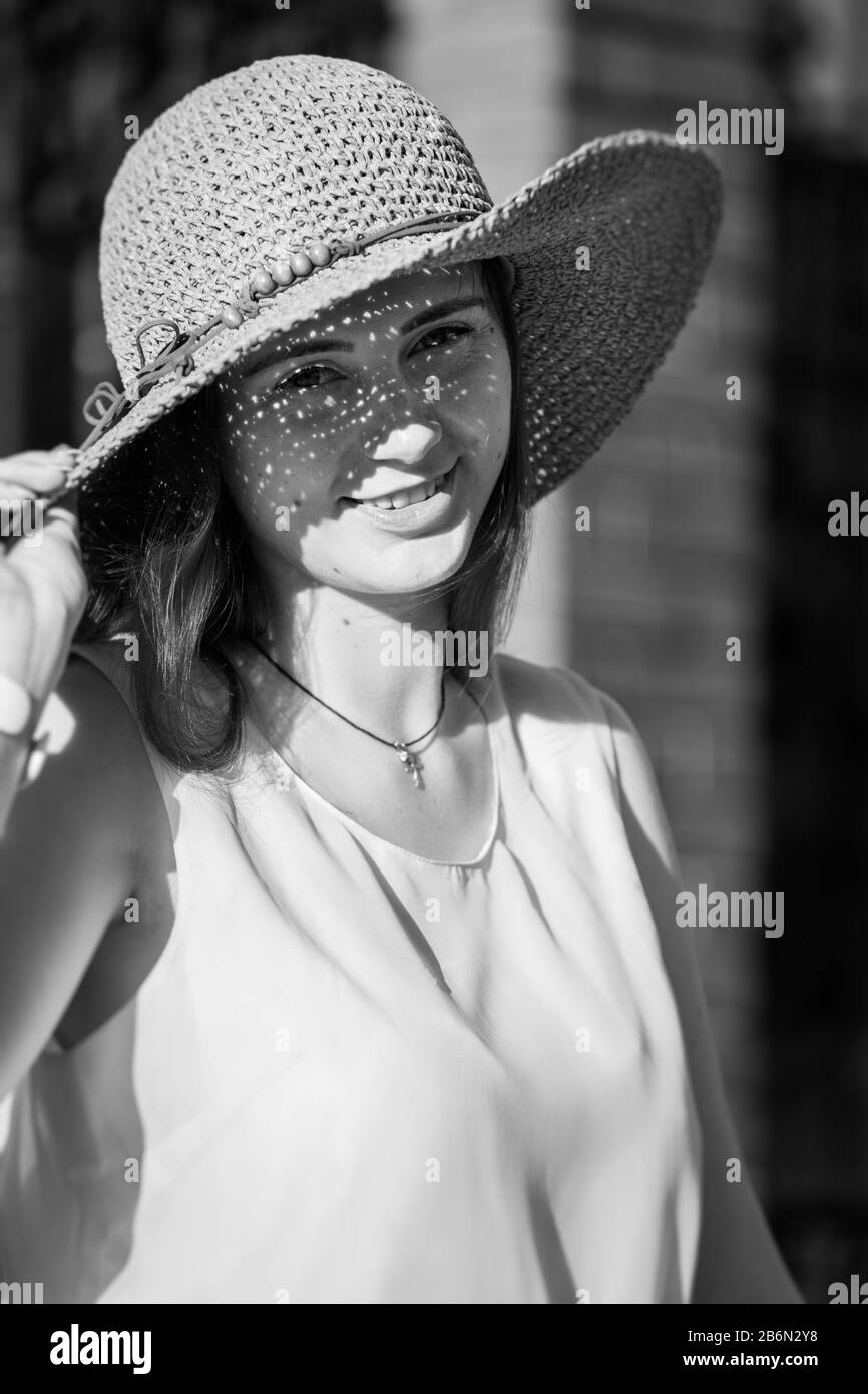 bella ragazza di capelli rossi in cappello di sole che guarda la macchina fotografica, sorridente, immagine monocromatica Foto Stock