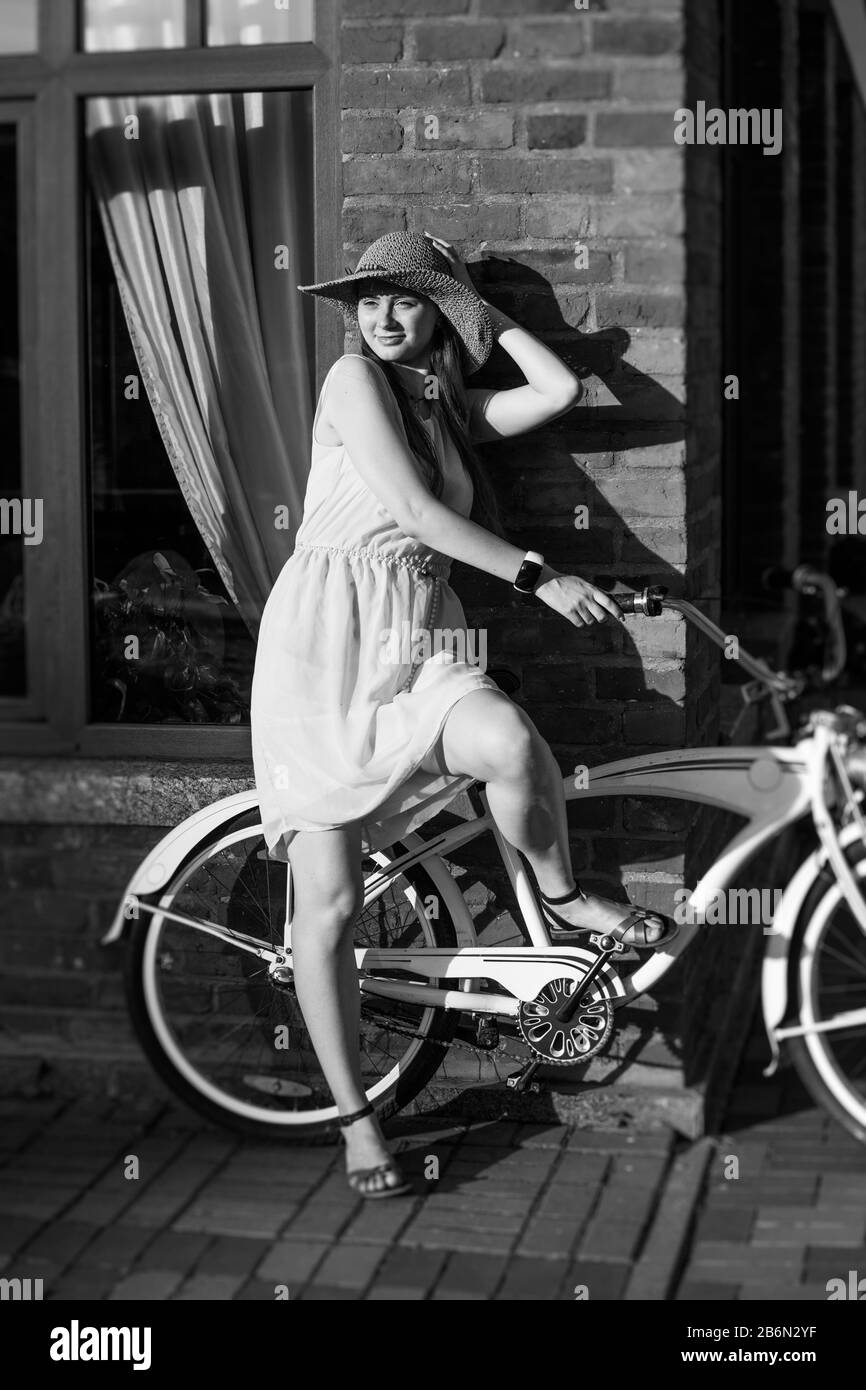 giovane capello rosso in cappello in piedi con la bici su strada soleggiata, monocromatico Foto Stock