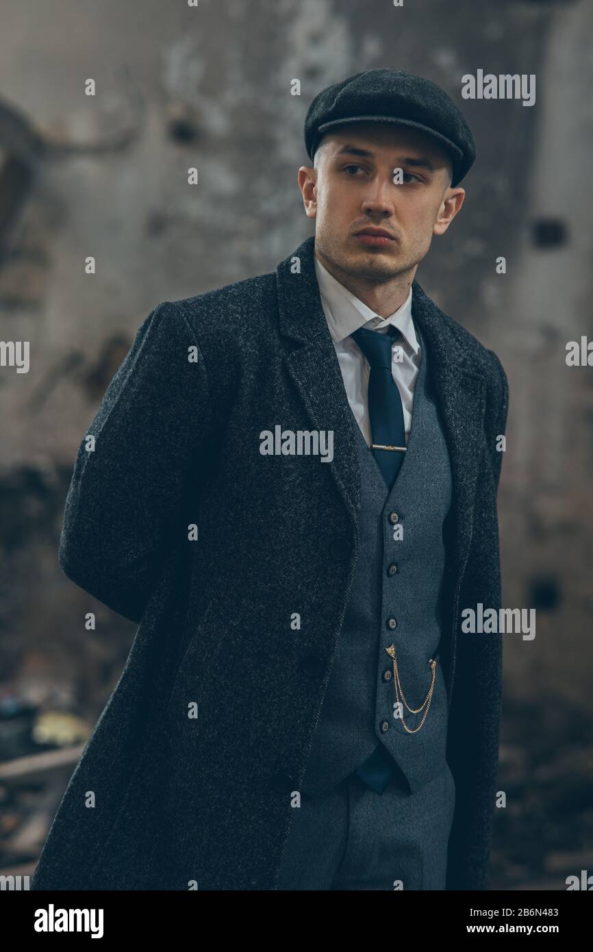 Un uomo che si posa nell'immagine di un gangster inglese retrò della 1920s  vestito con un cappotto, un abito e un cappuccio piatto in stile Spaky  blinders Foto stock - Alamy