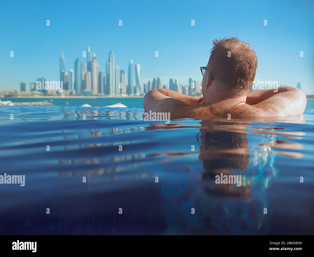 Ritratto di uomo rosso caucasico europeo rilassato con capelli indietro in occhiali in piscina sulla Dubai moderna (Emirati Arabi Uniti) e bac mare Foto Stock