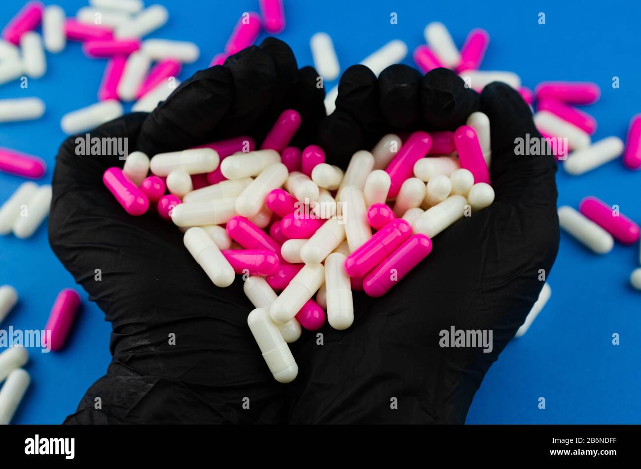 Due mani in guanti medici neri che tengono una manciata di capsule o farmaci come simbolo amore Foto Stock