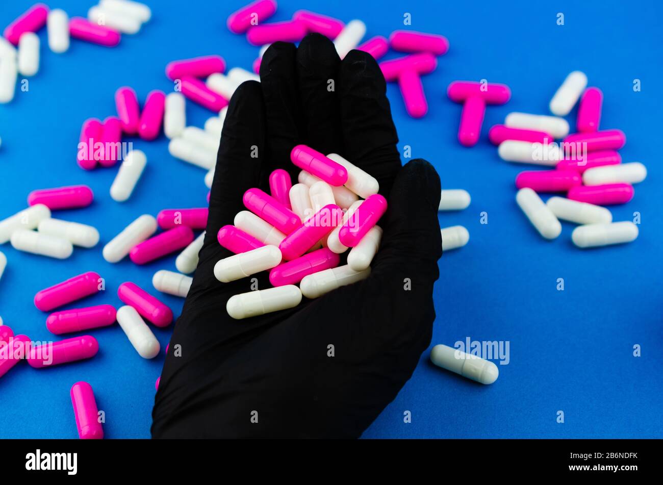 Una mano in un guanto medico nero contiene una manciata di capsule o farmaci Foto Stock