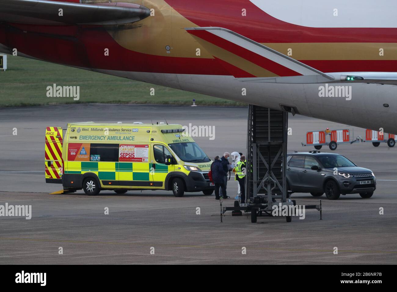 Un membro del NHS West Midlands Ambulance Service, indossando indumenti protettivi e una maschera facciale, parla ai passeggeri (a sinistra) dalla nave da crociera Grand Princess, colpita dal coronavirus, dopo che sono arrivati all'aeroporto di Birmingham dopo il loro rimpatrio nel Regno Unito dagli Stati Uniti. Foto PA. Data Immagine: Mercoledì 11 Marzo 2020. Circa 140 vacanzieri britannici erano stati bloccati sulla nave al largo della costa occidentale dell'America dopo che 21 persone hanno provato positivo per il virus a bordo. Vedi la storia PA SALUTE Coronavirru. Photo credit dovrebbe leggere: Steve Parsons/PA Wire Foto Stock