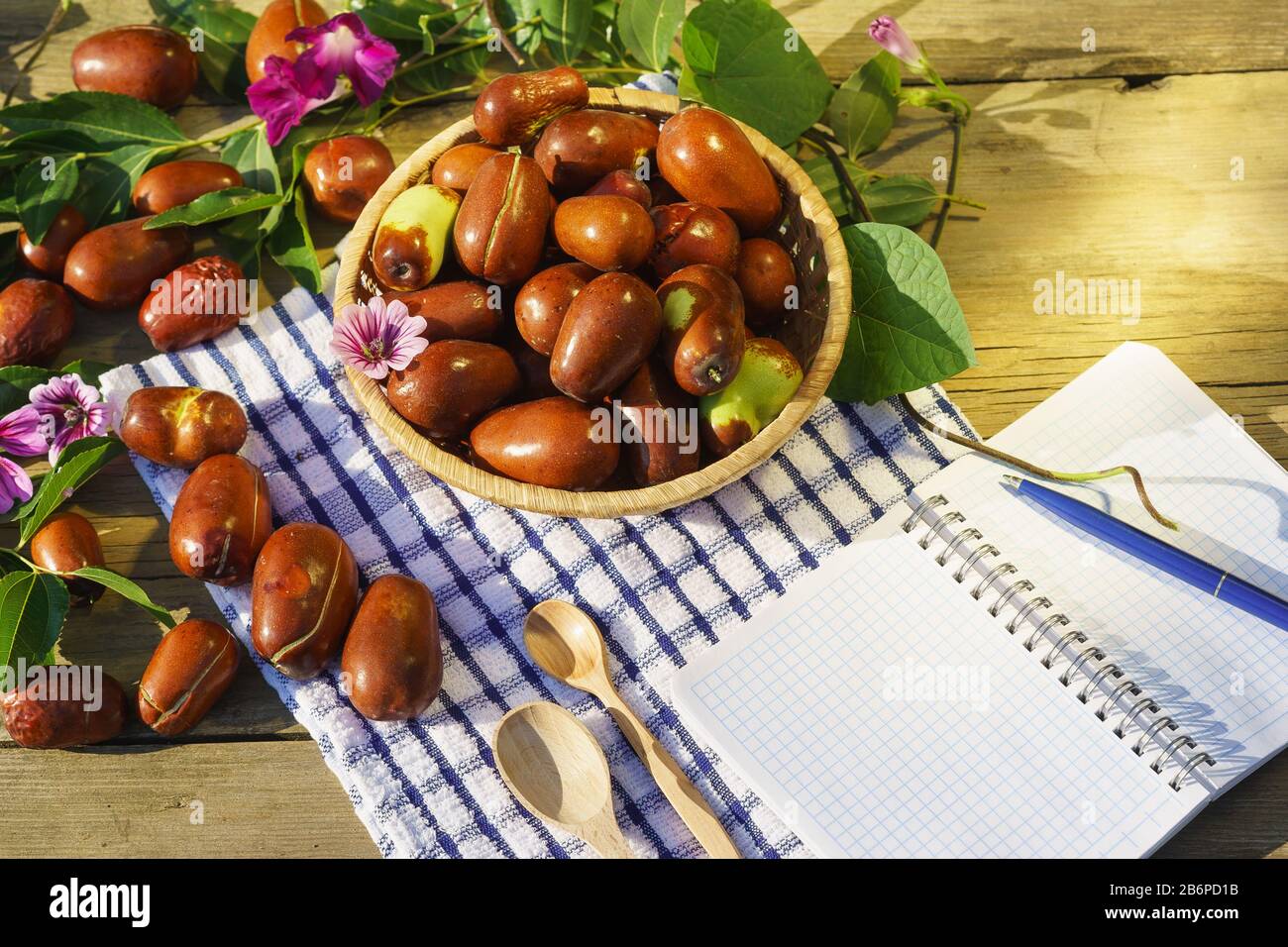 Cesto di vimini con frutti di Ziziphus reali, ciottoli, unabi, capiente, marmellata, capiinit, jojoba, dade cinese e blocco note per la scrittura alla luce del sole. Foto Stock