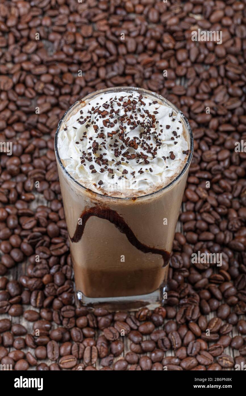 Frittelle di caffè freddo (frappuccino), con panna montata e sciroppo al caramello, con cannucce e grani di caffè su un tavolo di legno, spazio copia. Foto Stock