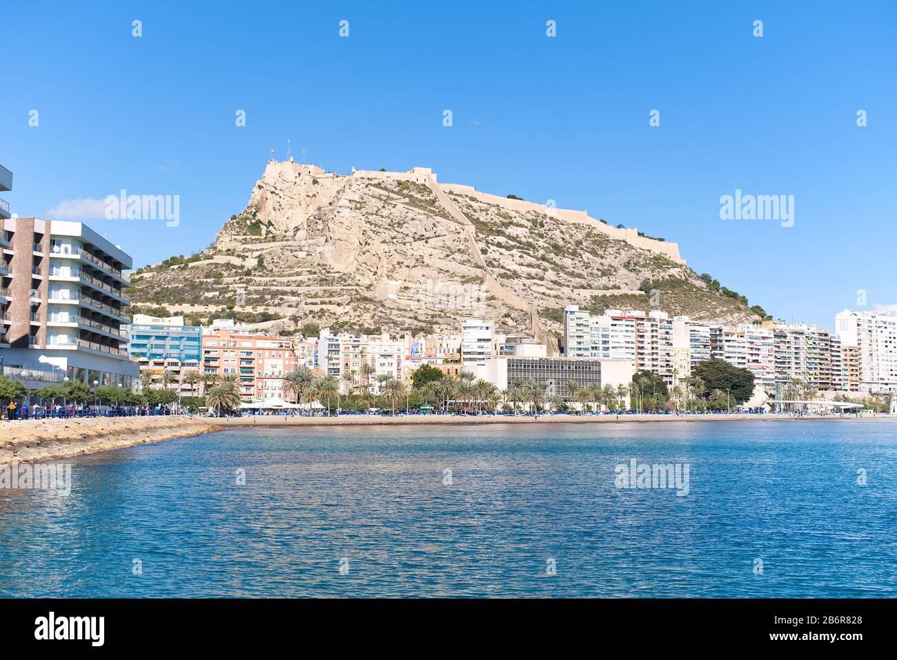 Vista del Castello di Santa Barbara situato sul Monte Benacantil dalla spiaggia sulla costa di Alicante sul Mar Mediterraneo in una luminosa giornata di sole blu chiaro. Foto Stock