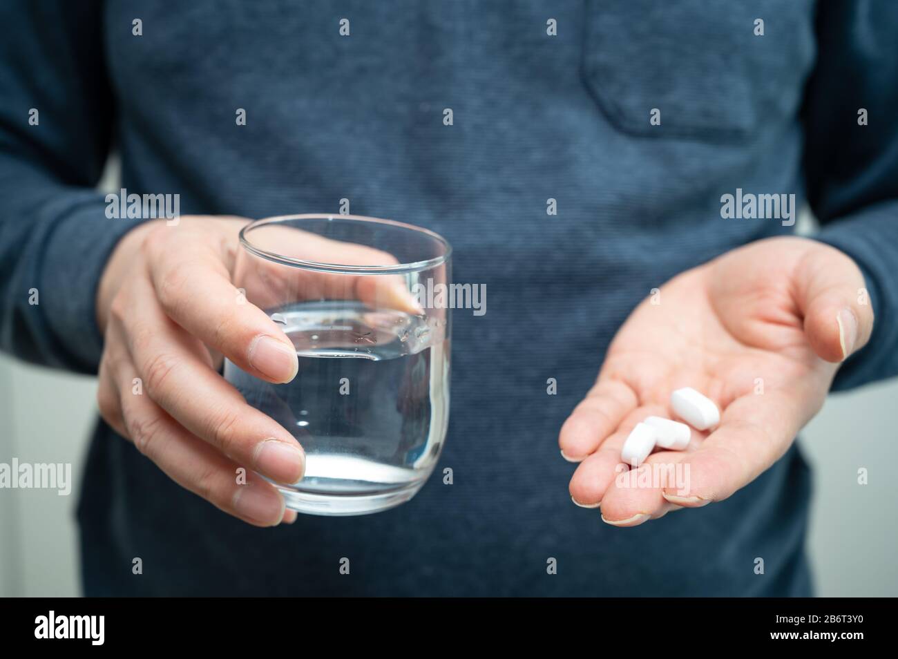 Termometro digitale e pillole bianche e bicchiere di vetro una mano dell'uomo che tiene una pillola bianca e una tazza di acqua in mano. Epidemia, antidolorifici, sanità e. Foto Stock