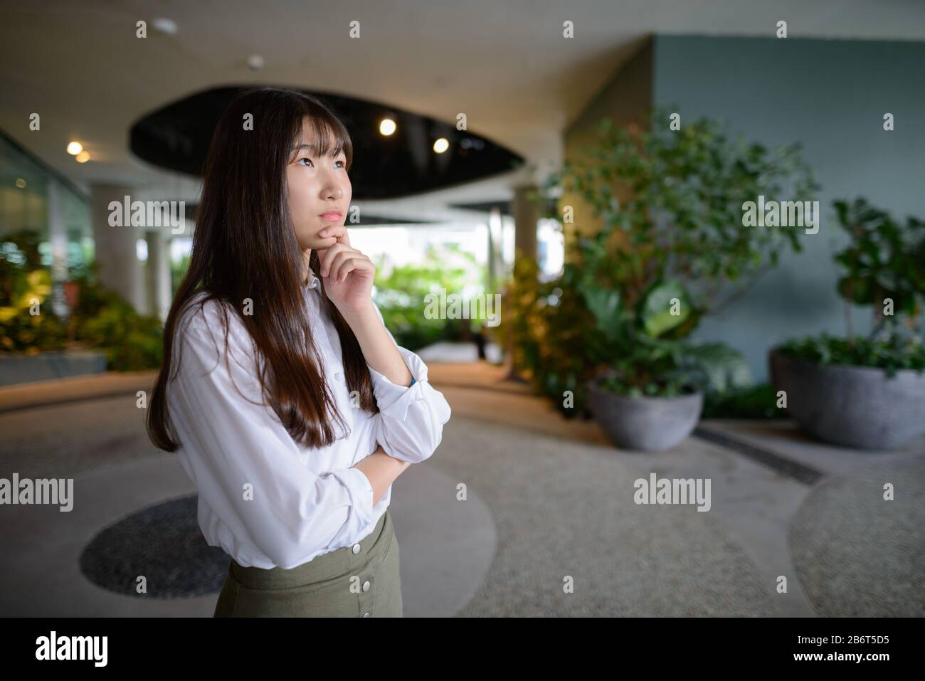 Giovane bella ragazza asiatica che pensa al giardino interno Foto Stock
