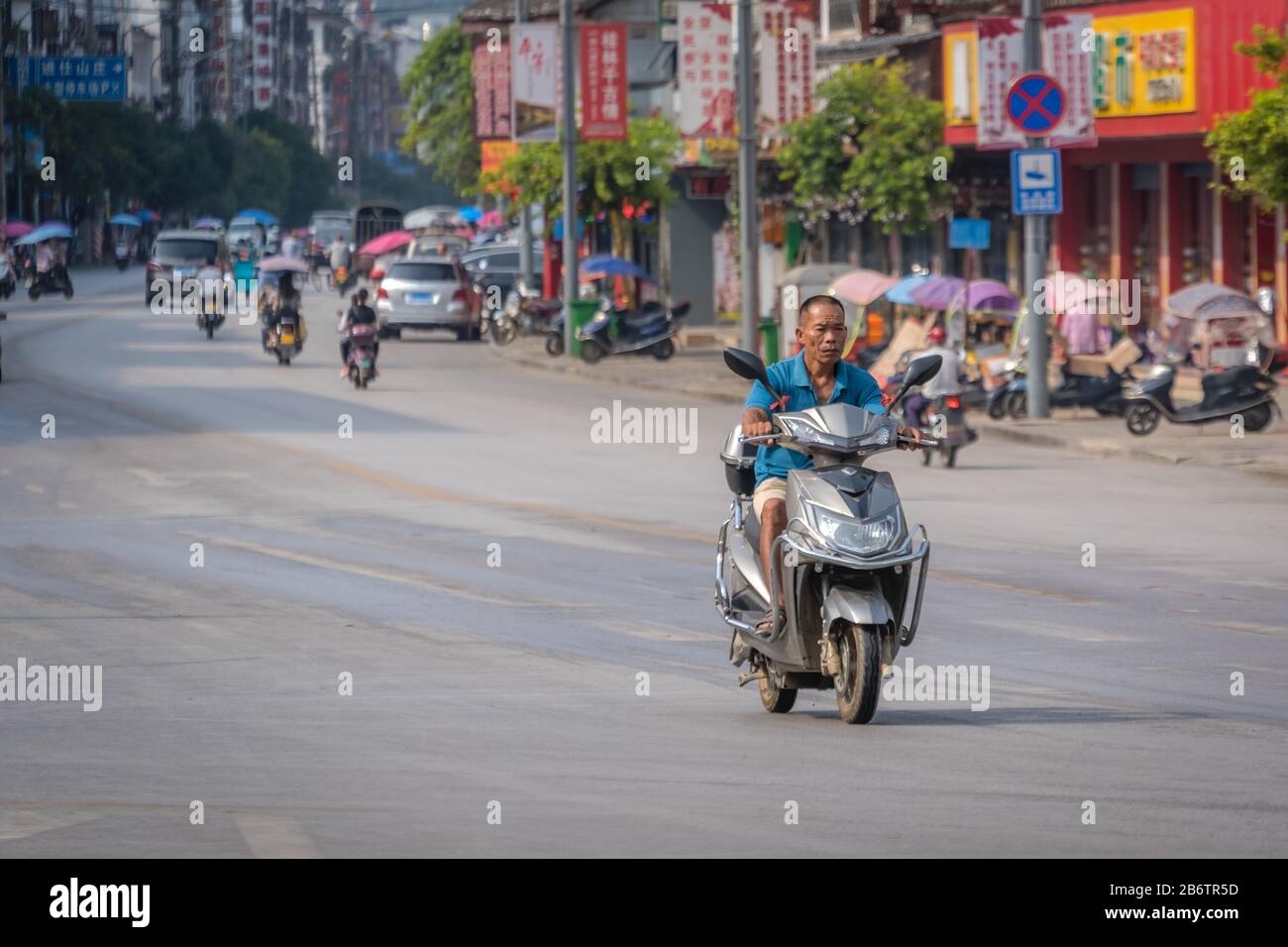 Yangshuo, Cina - Agosto 2019 : uomo Anziano che guida su uno scooter su una strada larga nella città di Yangshuo, provincia di Guangxi Foto Stock