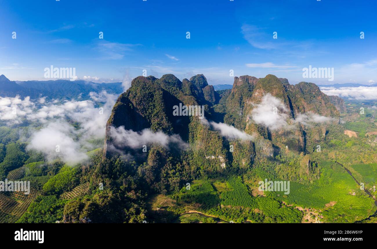 Panorama aereo di nube e nebbia che si sgonfano intorno a torreggianti montagne coperte di verde, giungla tropicale. Foto Stock