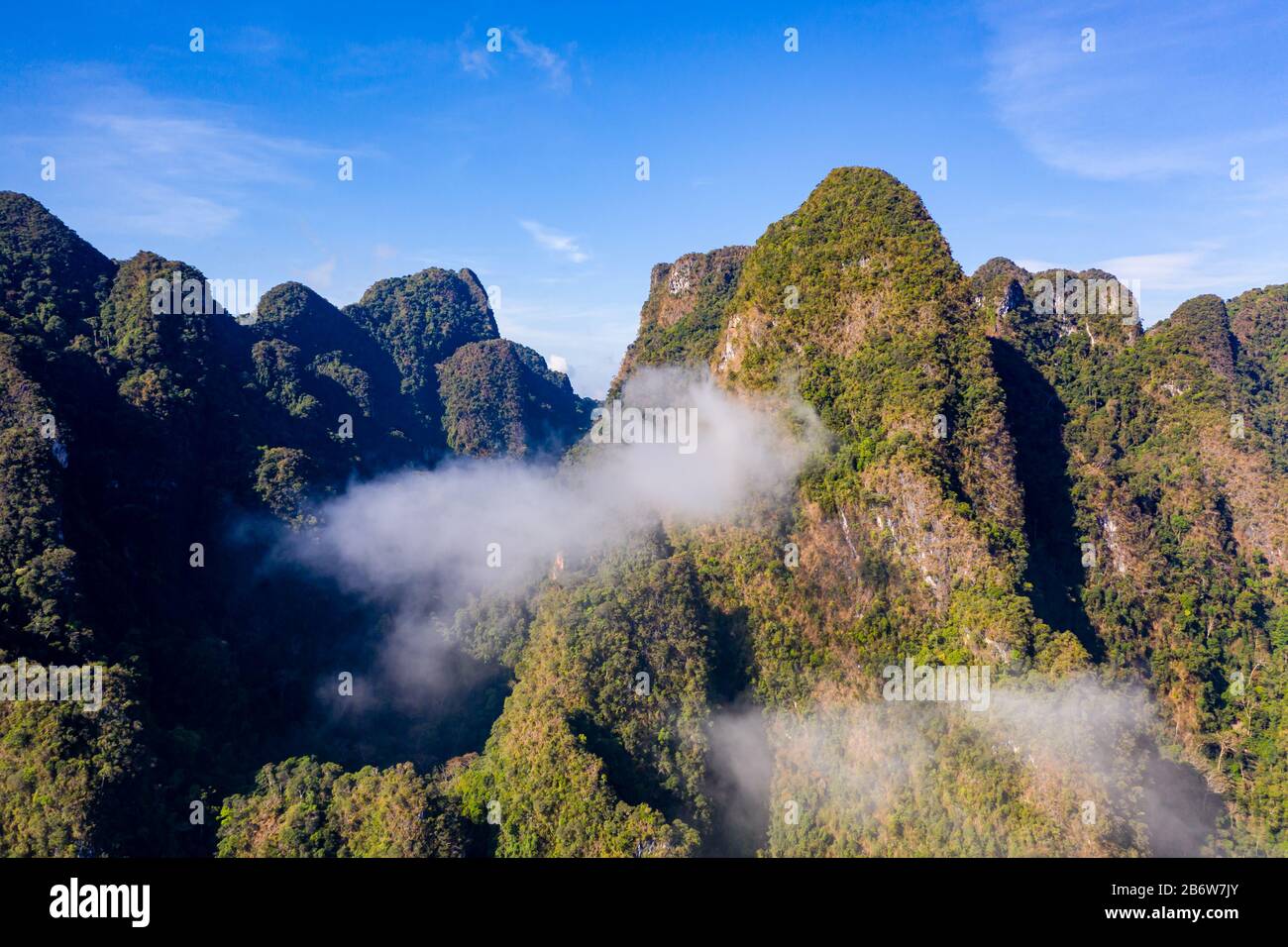 Vista aerea delle nuvole e della nebbia che si sgocciolano accanto alle torreggianti montagne calcaree coperte dalla giungla Foto Stock