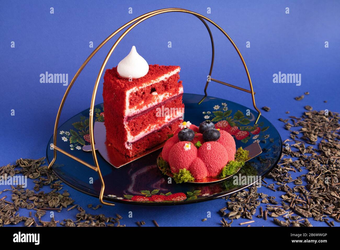 Due deliziose torte rosse appetitose su un piatto di vetro con tè verde secco sparso su sfondo viola Foto Stock
