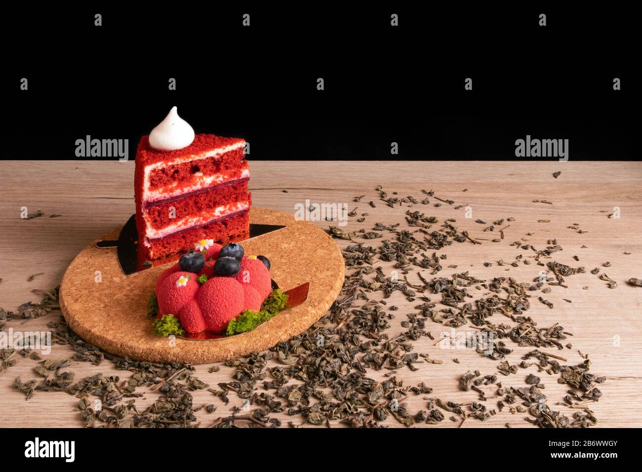 Due deliziose torte rosse appetitose su un supporto in sughero con tè verde secco sparso Foto Stock
