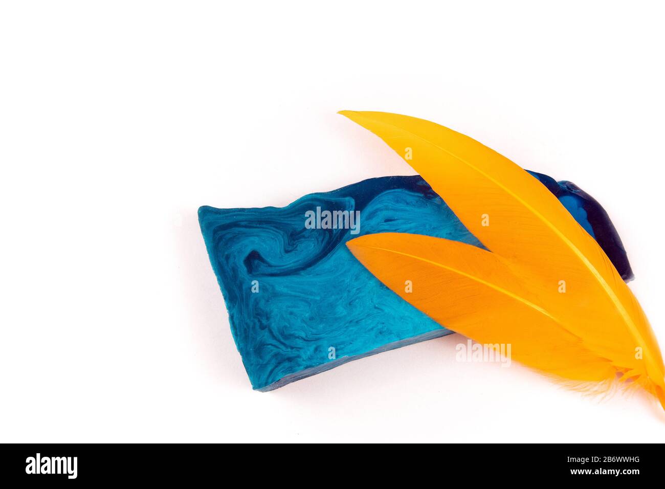 Sottile pezzo piatto di sapone alla menta blu fatto a mano e due piume arancioni isolato su sfondo bianco Foto Stock