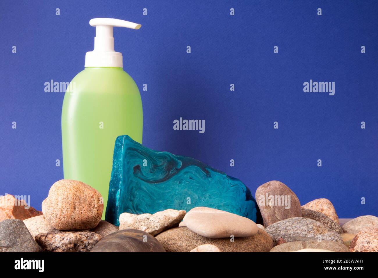 Sottile pezzo piatto di sapone alla menta blu fatto a mano che giace su ciottoli e toilette dietro Foto Stock