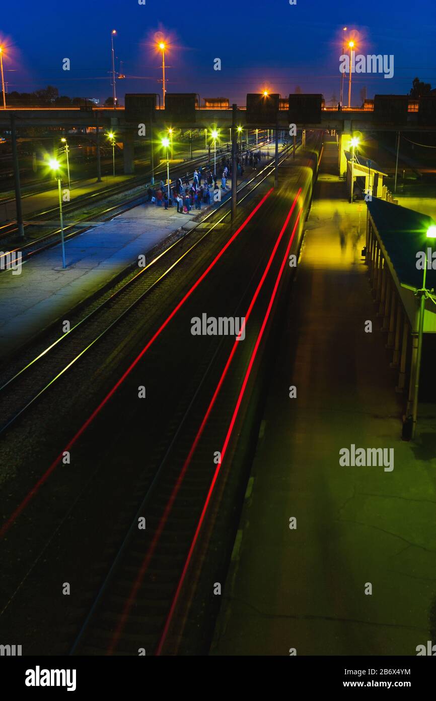La gente aspetta il treno alla stazione ferroviaria suburbana vicino al ponte la sera a riga. Zemitana Foto Stock