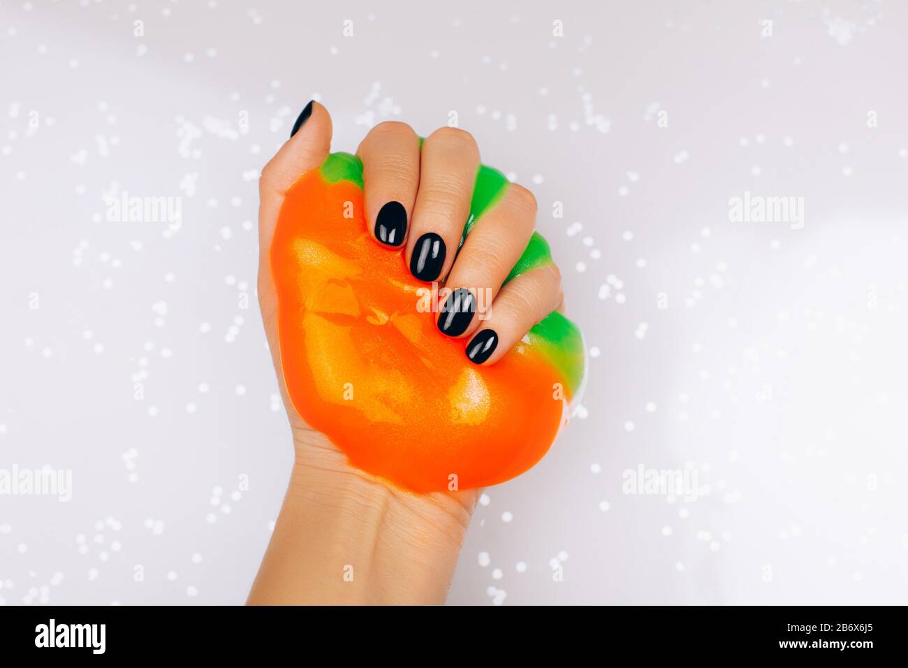mani con manicure nero che tiene la calce in arancione e verde vibrante colori Foto Stock