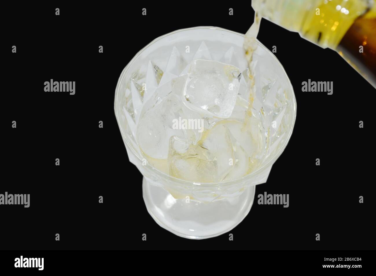 versare il whiskey dalla bottiglia su ghiaccio su fondo nero Foto Stock