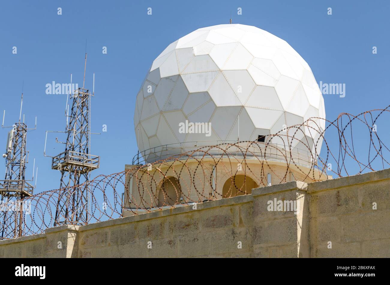 Cupola radar per aerei dietro il filo di ferro e muro di pietra con cielo blu sullo sfondo Foto Stock