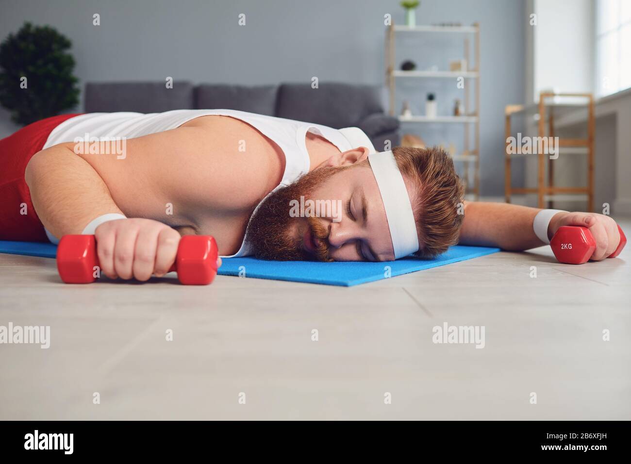 Un uomo pigro grasso si trova con manubri sul pavimento della casa. Foto Stock