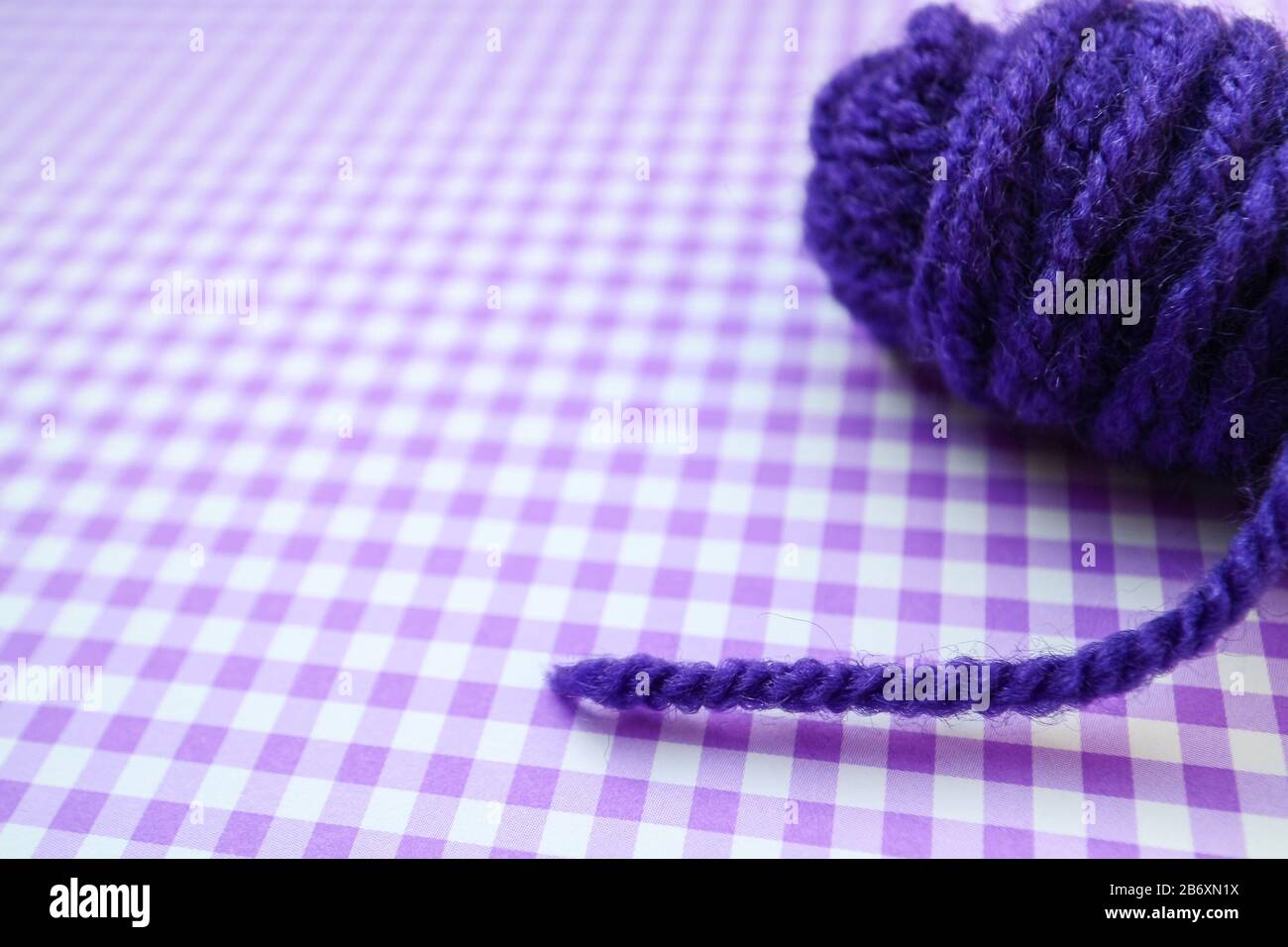 Palla di filato viola su uno sfondo a scacchi viola. Foto Stock