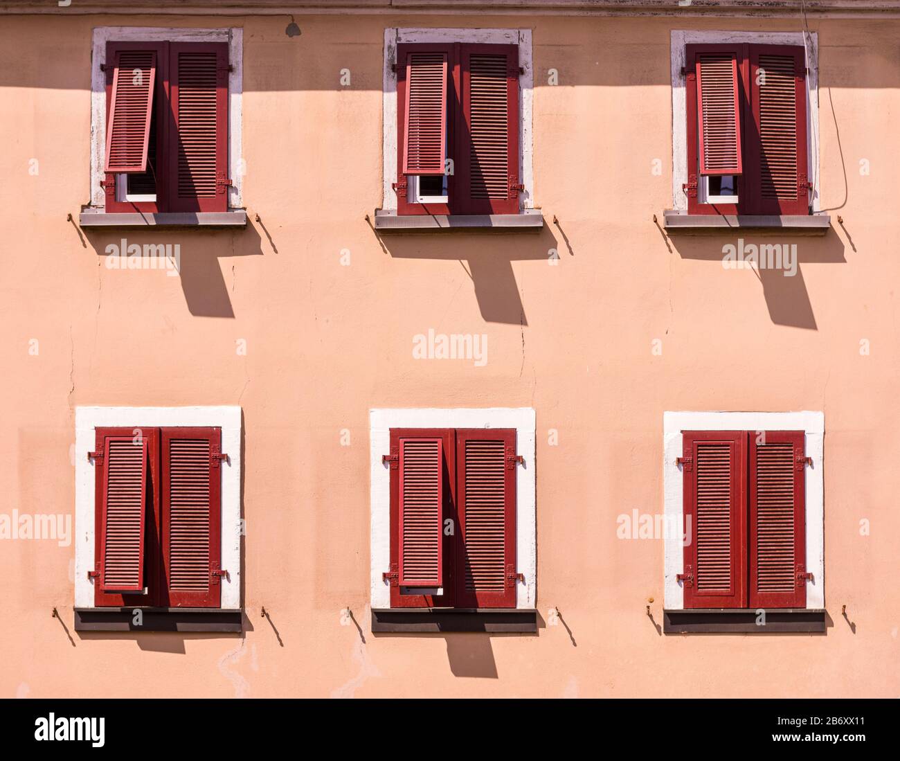 Facciata di una casa in stile mediterraneo, intonaco dipinto in color sabbia con persiane chiuse in legno rosso scuro, parzialmente esposto su 6 finestre Foto Stock