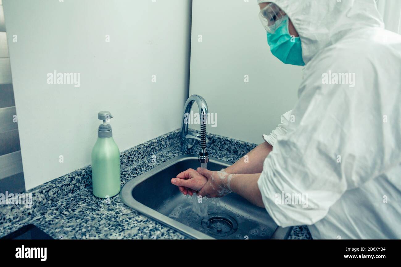 Donna in tuta di protezione batteriologica lavando le mani Foto Stock