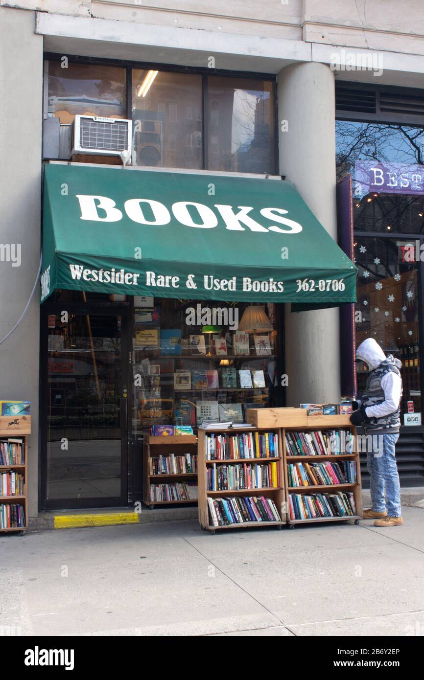 un uomo cerca pile di libri sul marciapiede di fronte a un venditore di libri indipendente usato sul lato ovest superiore di manhattan Foto Stock