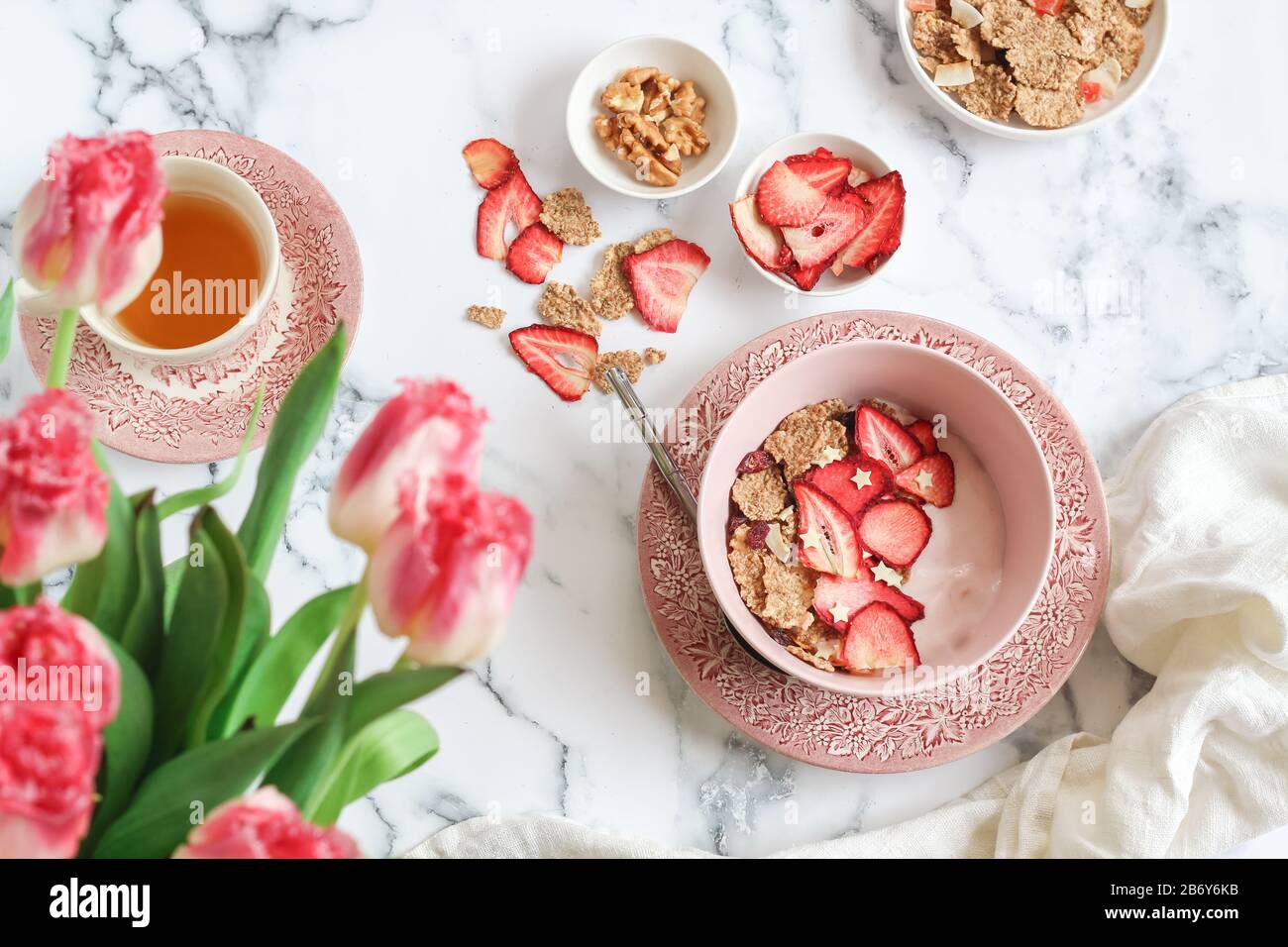 Scena della colazione con yogurt, muesli e fragole secche e una tazza di tè su un tavolo regolabile Foto Stock