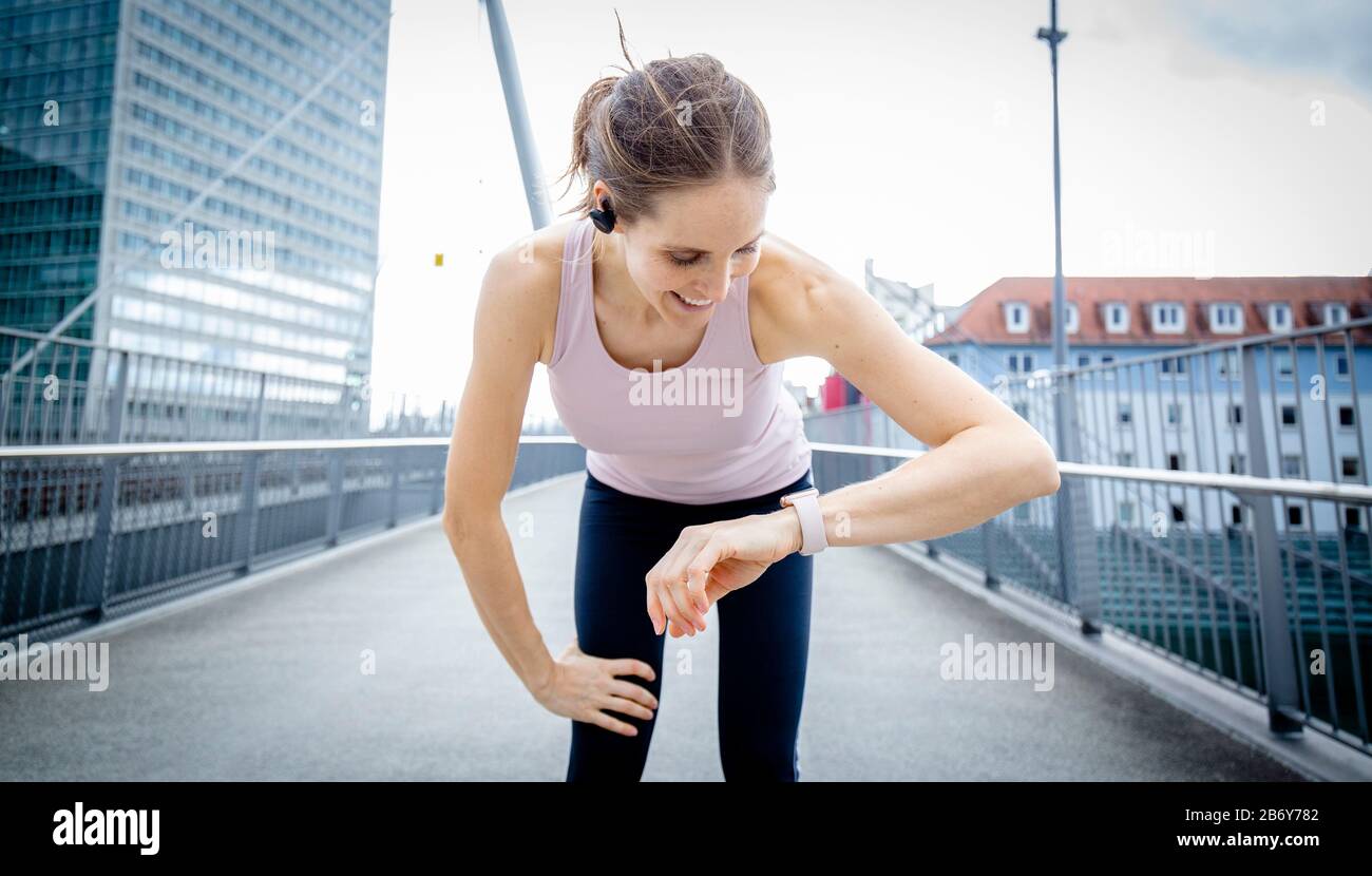 Sportliche Frau fängt ihren Atem nach dem Training während sie ihre Smartwatch überprüft. Femmina Runner che prende una pausa durante il suo jogging. Foto Stock