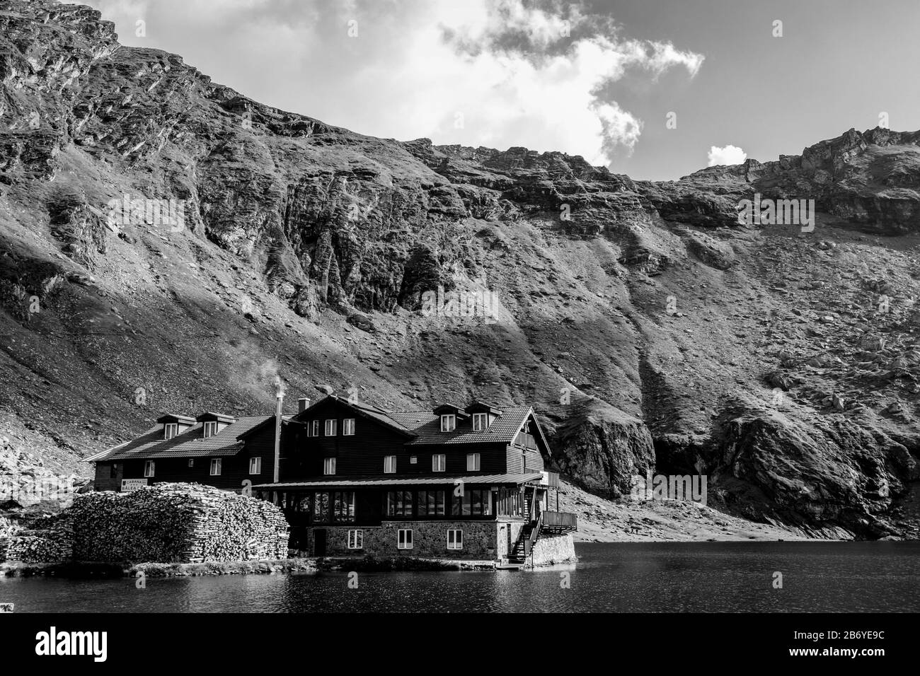 Composizione in bianco e nero di chalet di montagna su un lago di montagna con nuvole di montagna e puffy sullo sfondo Foto Stock