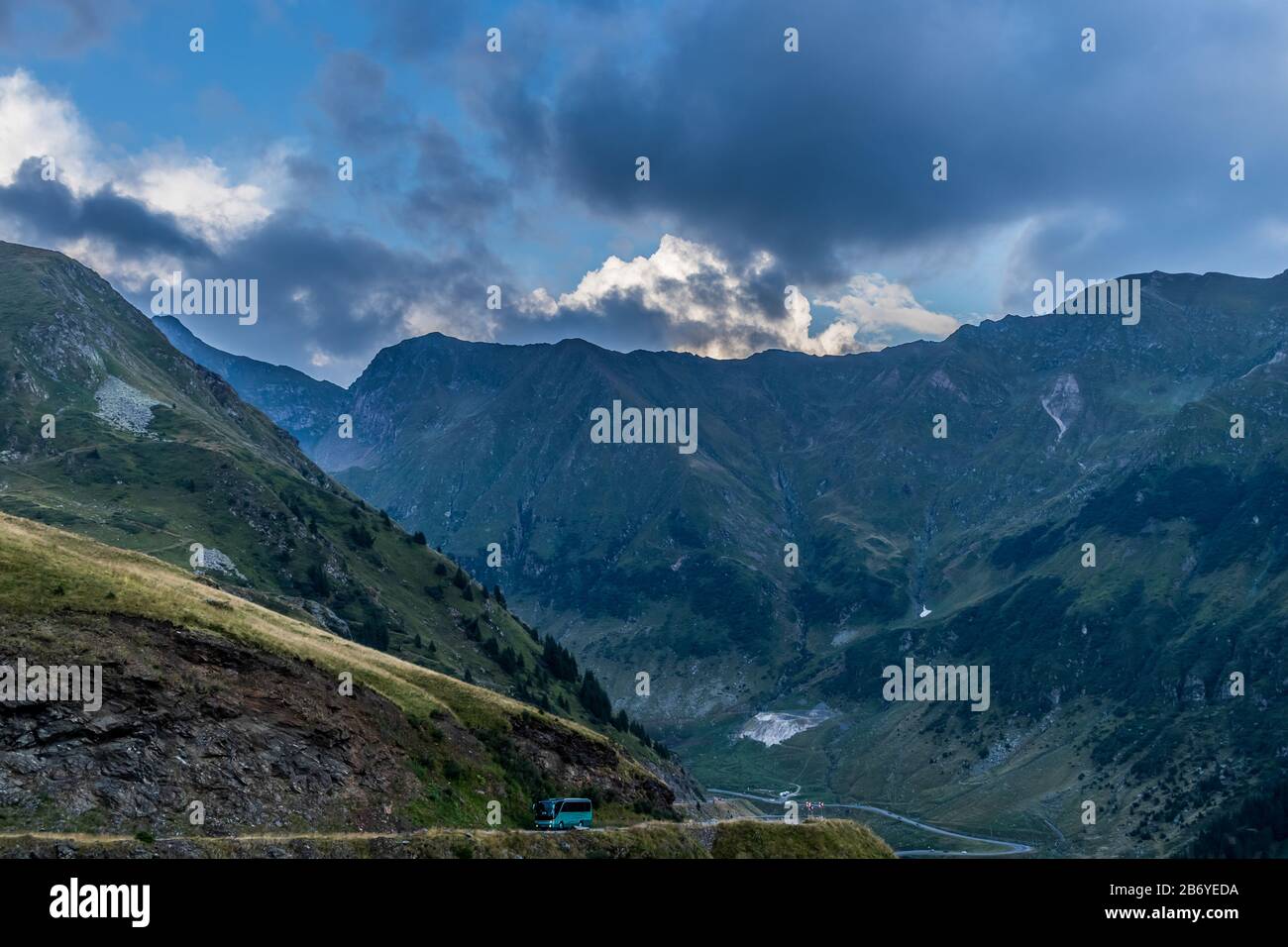 Autobus che passa su strada di montagna con montagne sullo sfondo e nuvole scure sopra Foto Stock
