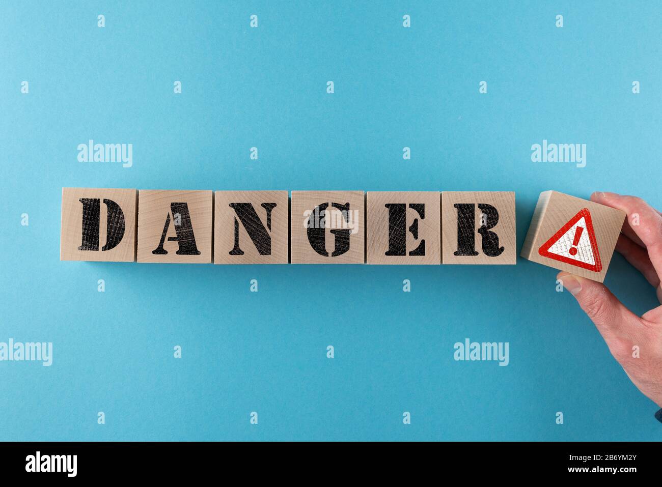 Pericolo di parola e segnale di avvertimento su cubi di legno su sfondo blu Foto Stock