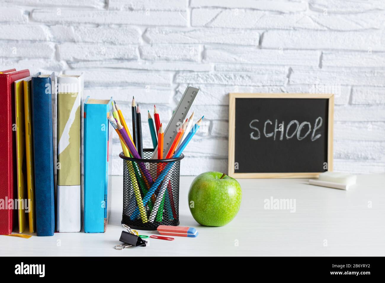 Torna a scuola con libri, matite colorate e mela su tavola bianca in legno. Orari della scuola. Istruzione. Foto Stock