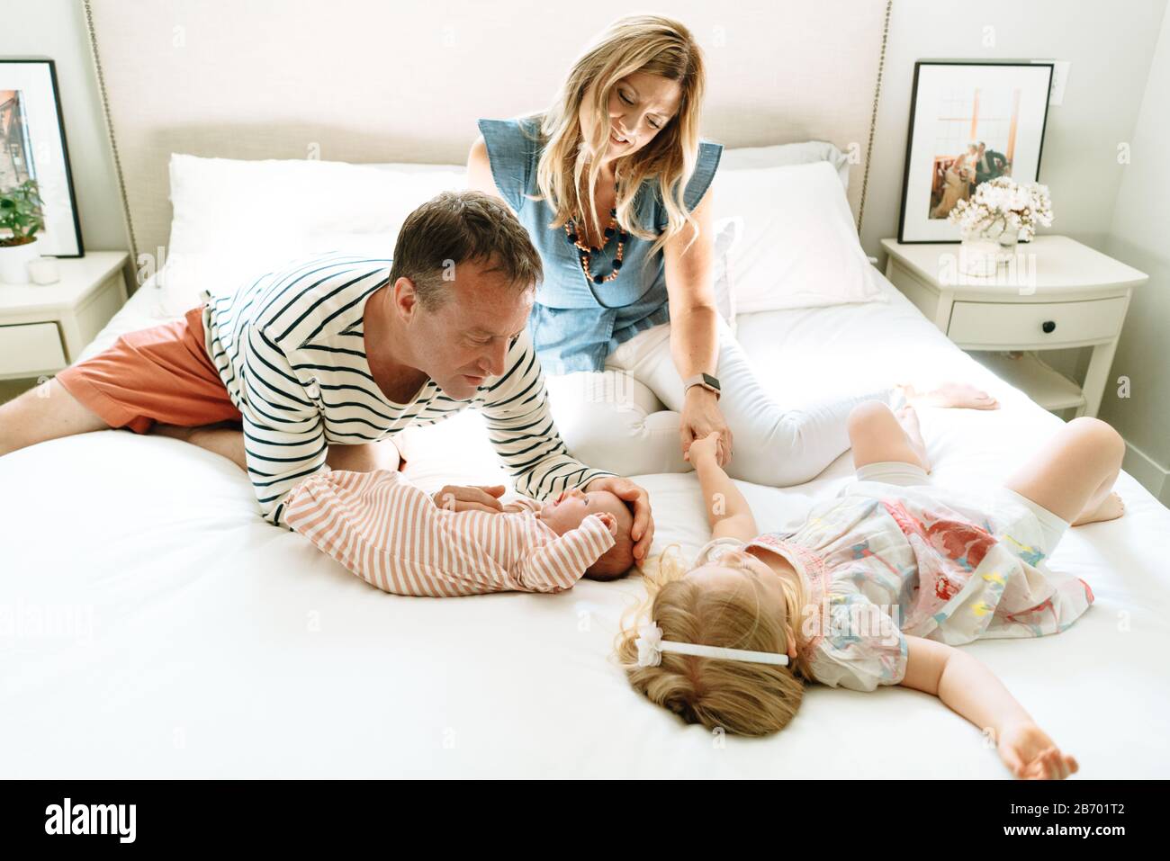 Madre e padre seduti su un letto insieme alle loro figlie Foto Stock