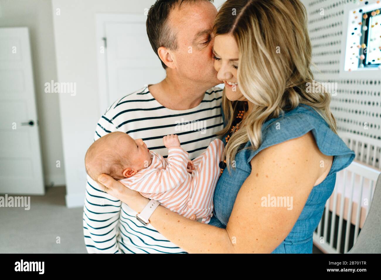 Un marito bacia la moglie sulla guancia mentre tiene un bambino Foto Stock