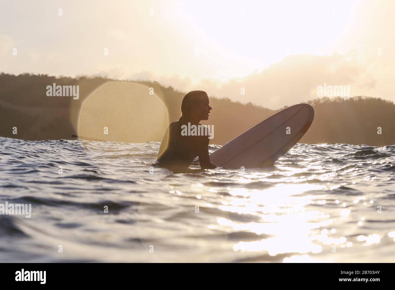 Surfista femminile nell'oceano al tramonto Foto Stock