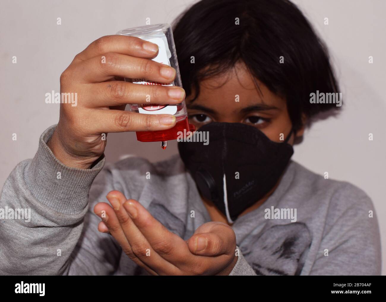 Un bambino indiano o un bambino che usa un disinfettante e indossa una maschera protettiva per la protezione contro l'epidemia di virus corona Foto Stock