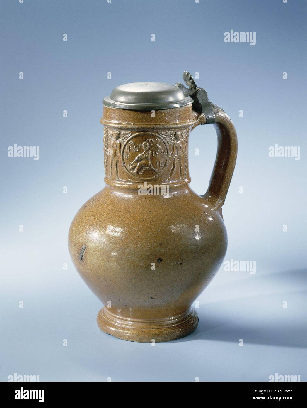 Kruik met het Christuskind in medaillons Kruik van steengoed op standring met een bolvormig lichaam en wijde nek. Het C-vormige o è vestigd aan de nek en de schouder. Profielen op de voet en nek. Bedekt Met een bruine engobe. Op de nek in reliëf twee gedrukte en opgelegde vakken met een medaillon gedragen door twee engelen. In het medaillon het Christuskind met het kruis en de opschriften 'IHS', 'G' in spiegelbeeld en '1574 IE'. Bevestigd aan het oor een tinnen montuur met een wapen aan de binnenzijde van de deksel. Raeren. Produttore : pottenbakker: Jan Emens Mennicken (vermeld op Foto Stock