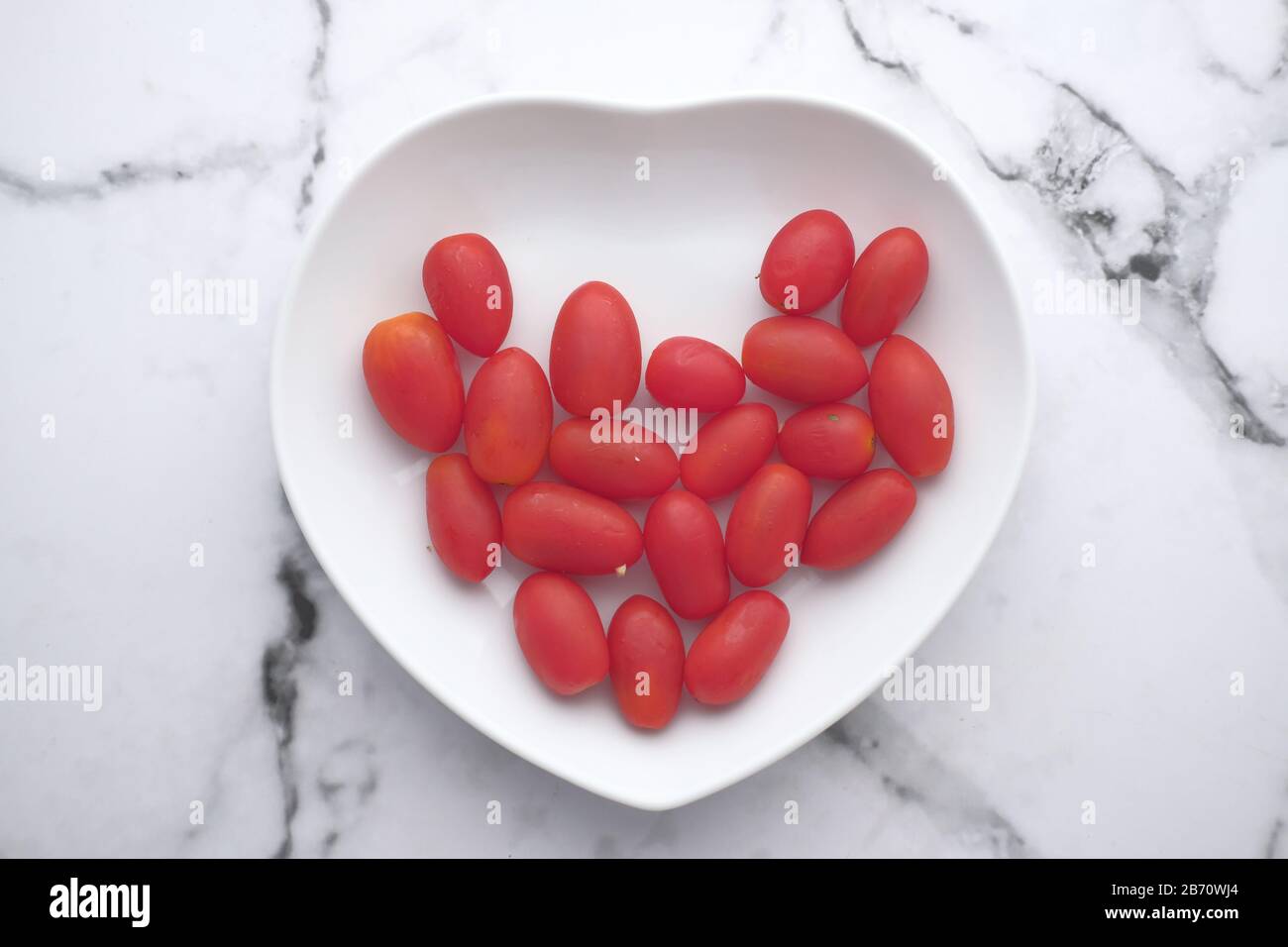 pomodoro fresco di ciliegio rosso su piatto a forma di cuore Foto Stock