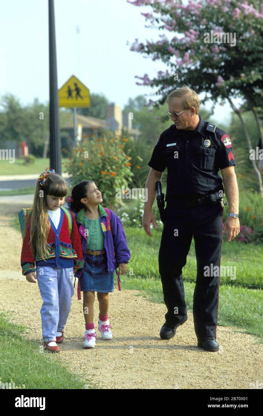 Austin Texas USA: Gli studenti dell'asilo camminano con l'ufficiale di polizia uniforme sulla via della casa dalla scuola. SIGNOR ©Bob Daemmrich Foto Stock
