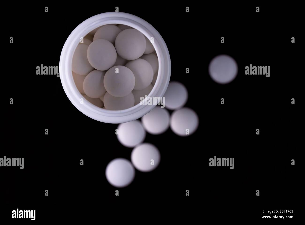 Sfondo nero. Un flacone bianco aperto all'interno di compresse rotonde bianche. Separare le compresse nella sfocatura. Vista dall'alto. Foto Stock
