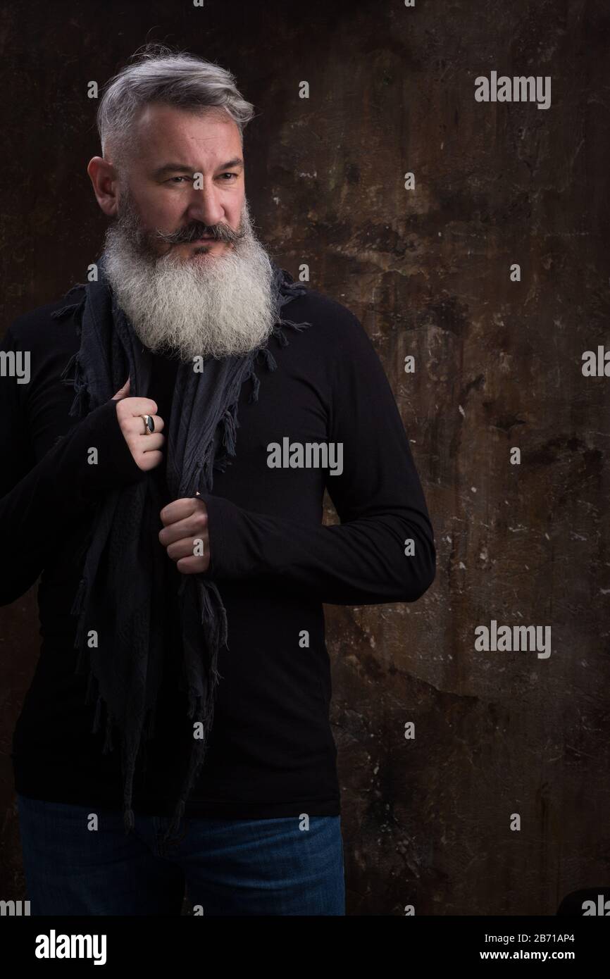 Studio ritratto di bello maturo grigio-capelli bearded uomo contro la parete scura, fuoco selettivo Foto Stock