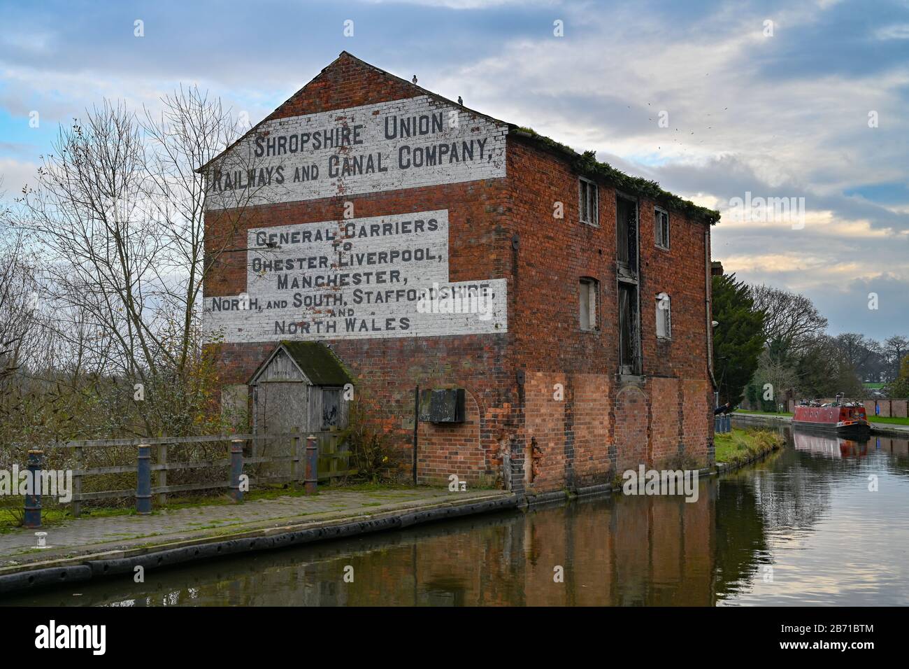 Vecchio edificio del canale fatiscente a Ellesmere Shropshire accanto al canale in una fredda e tranquilla giornata invernale con una barca a remi sullo sfondo. Foto Stock