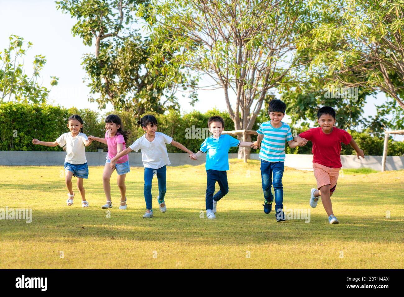 Grande gruppo di felice asiatico sorridente asilo bambini amici tenere le mani giocare e correre nel parco nella soleggiata giornata estiva in abiti casual. Foto Stock