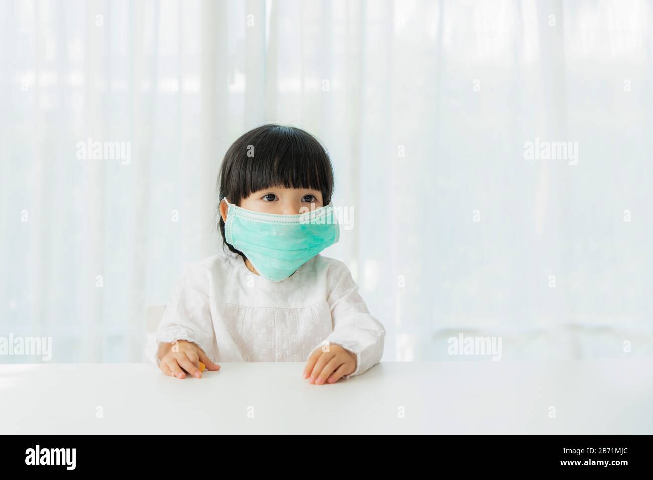 Piccola ragazza cinese che indossa una maschera sana del viso seduto in soggiorno a casa per prevenire la polvere PM2,5, smog, inquinamento dell'aria e COVID-19. Sanità conce Foto Stock