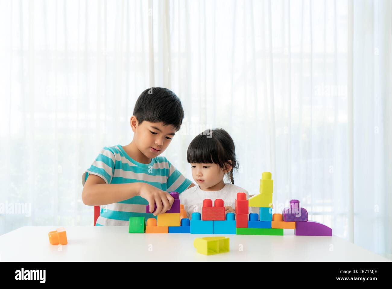 Asian fratello carino e sorella giocare con un giocattolo blocco designer sul tavolo in soggiorno a casa. Concetto di legame di fratello, amicizia e imparare Foto Stock