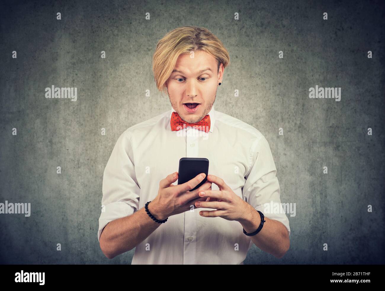 Uomo che guarda il suo smartphone con un'espressione sorpresa sul suo volto. Foto Stock