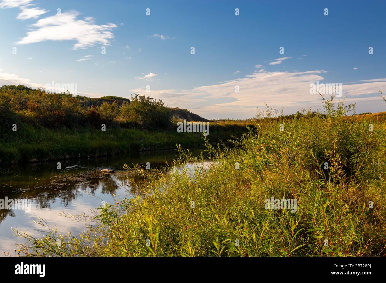 Un flusso tranquillo e pacifico che scorre attraverso una valle nella campagna rurale lato delle praterie Saskatchewan in Canada con il cielo che si riflette nell'acqua Foto Stock